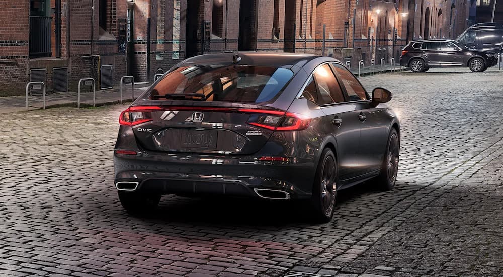 Grey 2024 Honda Civic Hatchback Sport driving on a stone street.