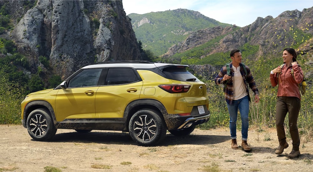 People walking from a yellow 2026 Chevy Trailblazer parked off-road.