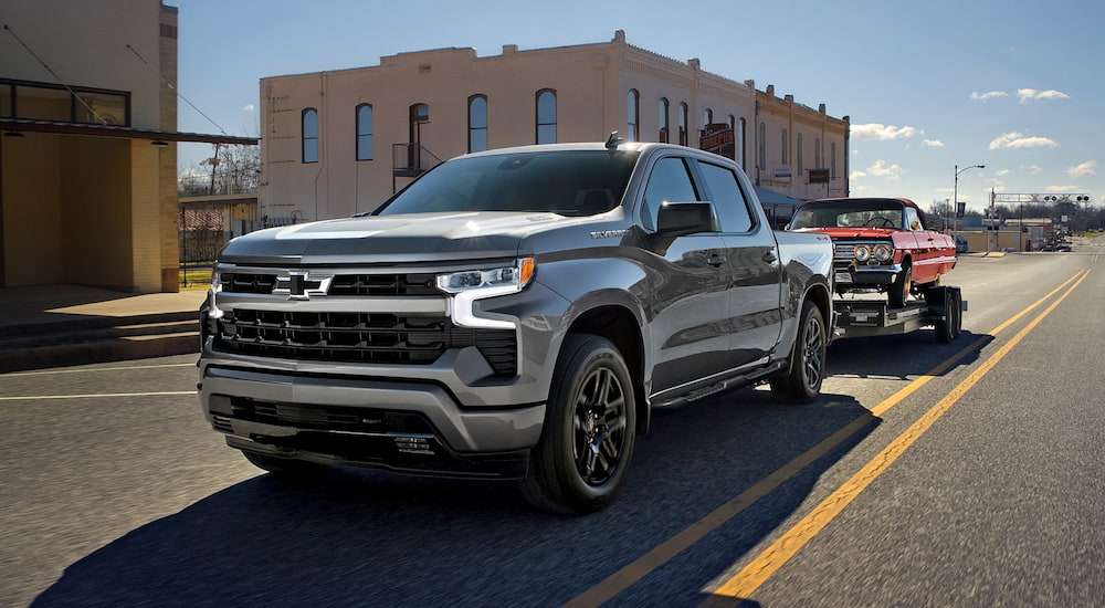 Silver 2026 Chevy Silverado 1500 driving down an open road from a car dealership.
