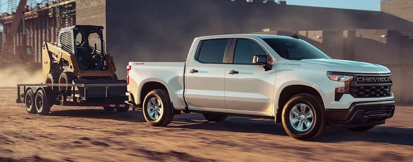 A white 2023 Chevy Silverado 1500 Custom is shown towing a trailer.