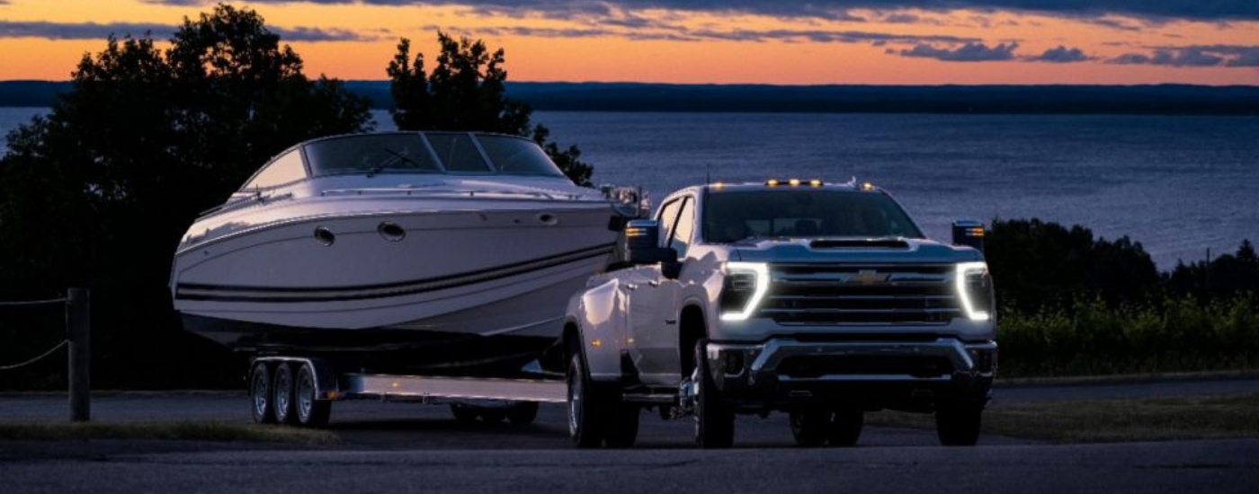 White 2025 Cheevy Silverado 3500 towing a boat at dusk