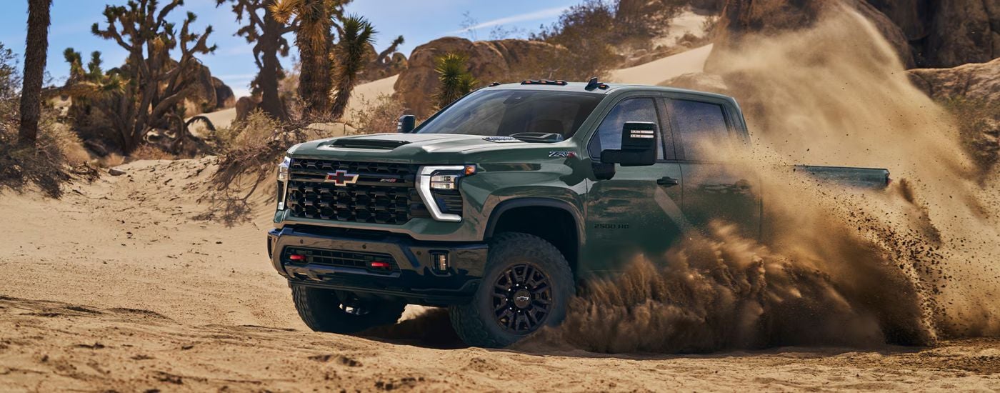 Green 2026 Chevy Silverado 2500 HD driving off-road and kicking up dust.