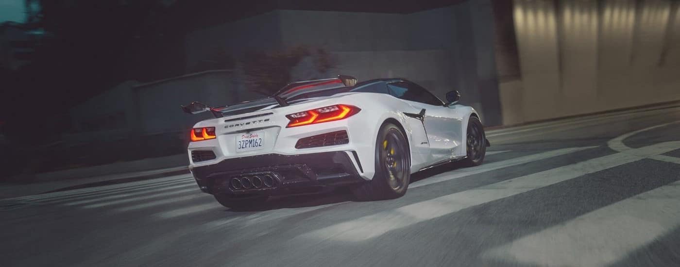 A white 2024 Chevy Corvette Z06 is shown rounding a corner after leaving a Chevy dealer.