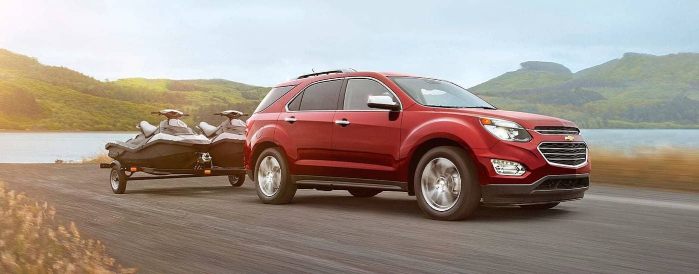 A red 2016 Chevy Equinox is shown towing jet skis near a lake.