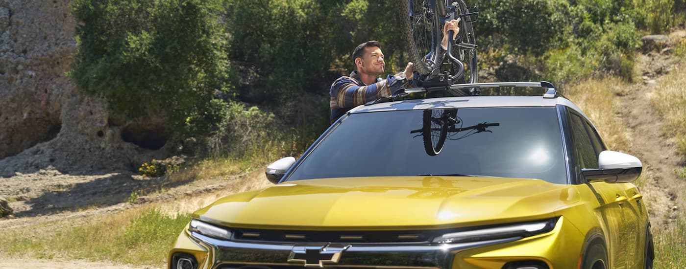 A man loading a bicycle into the bed onto the roof of a 2025 Chevy Trailblazer ACTIV.
