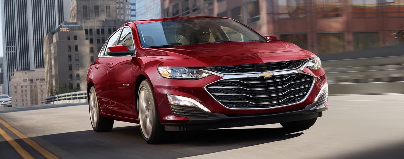 A red 2024 Chevy Malibu driving to a Chevy dealer near Saline.